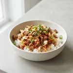 Egg roll in a bowl with ground pork, cabbage, carrots, rice, green onions, and Sriracha