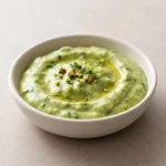 Creamy green sauce with avocado, lime, herbs, and pistachios in a ceramic bowl