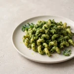 Vegan kale pesto coating pasta on a plate with visible almond flecks and fresh green texture