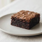 Fudgy espresso brownie square with a crackled top and dense cocoa interior on a ceramic plate