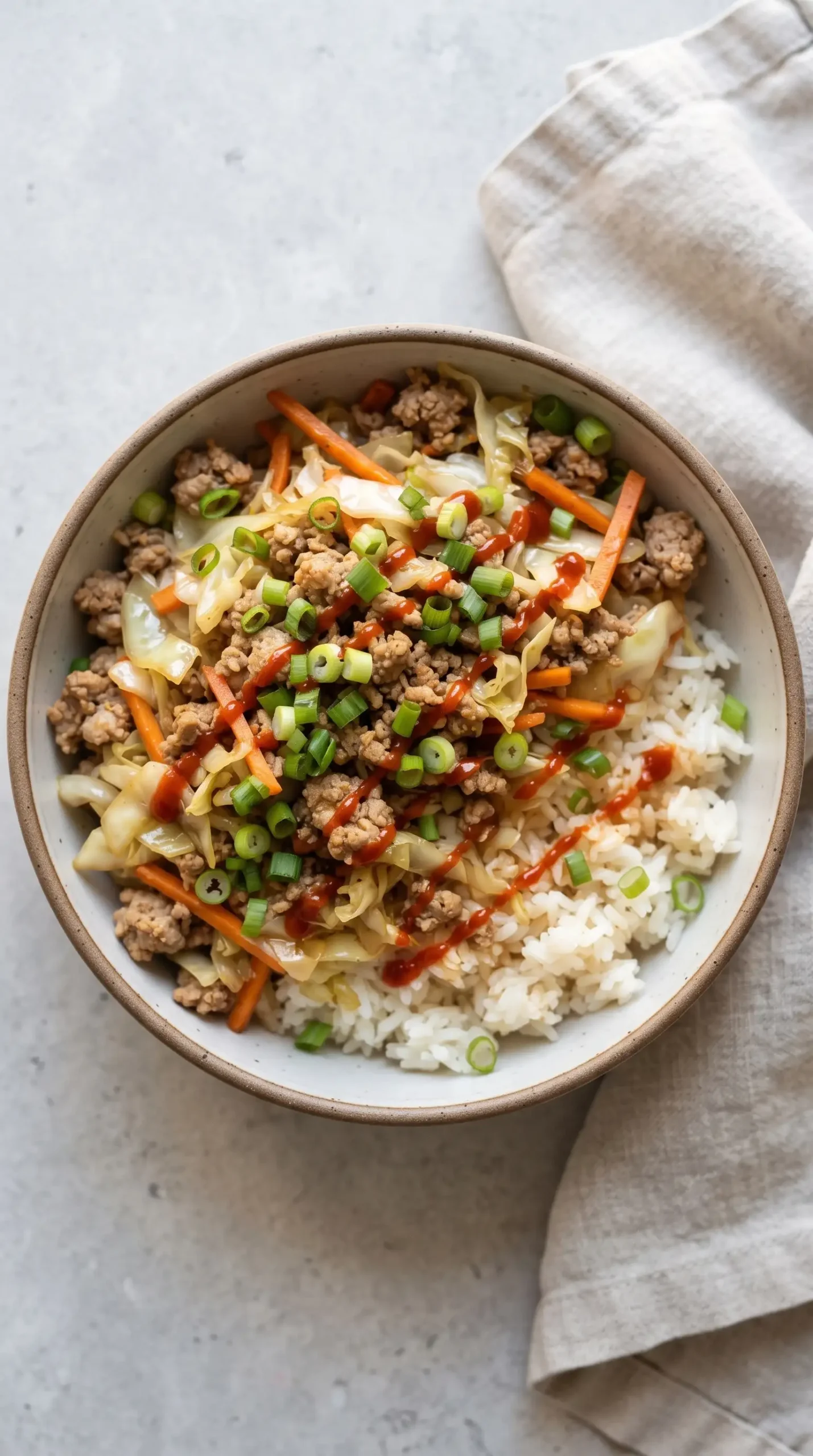Finished egg roll in a bowl served over rice with green onions and Sriracha