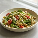 Lemon pesto penne with roasted tomatoes, baby broccoli, basil, and feta in a bowl