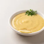 Bowl of creamy sunshine sauce with olive oil and dried herbs on a light surface