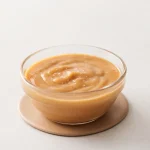 Vegan caramel sauce in a glass bowl with a smooth glossy maple and almond butter texture