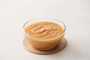 Vegan caramel sauce in a glass bowl with a smooth glossy maple and almond butter texture